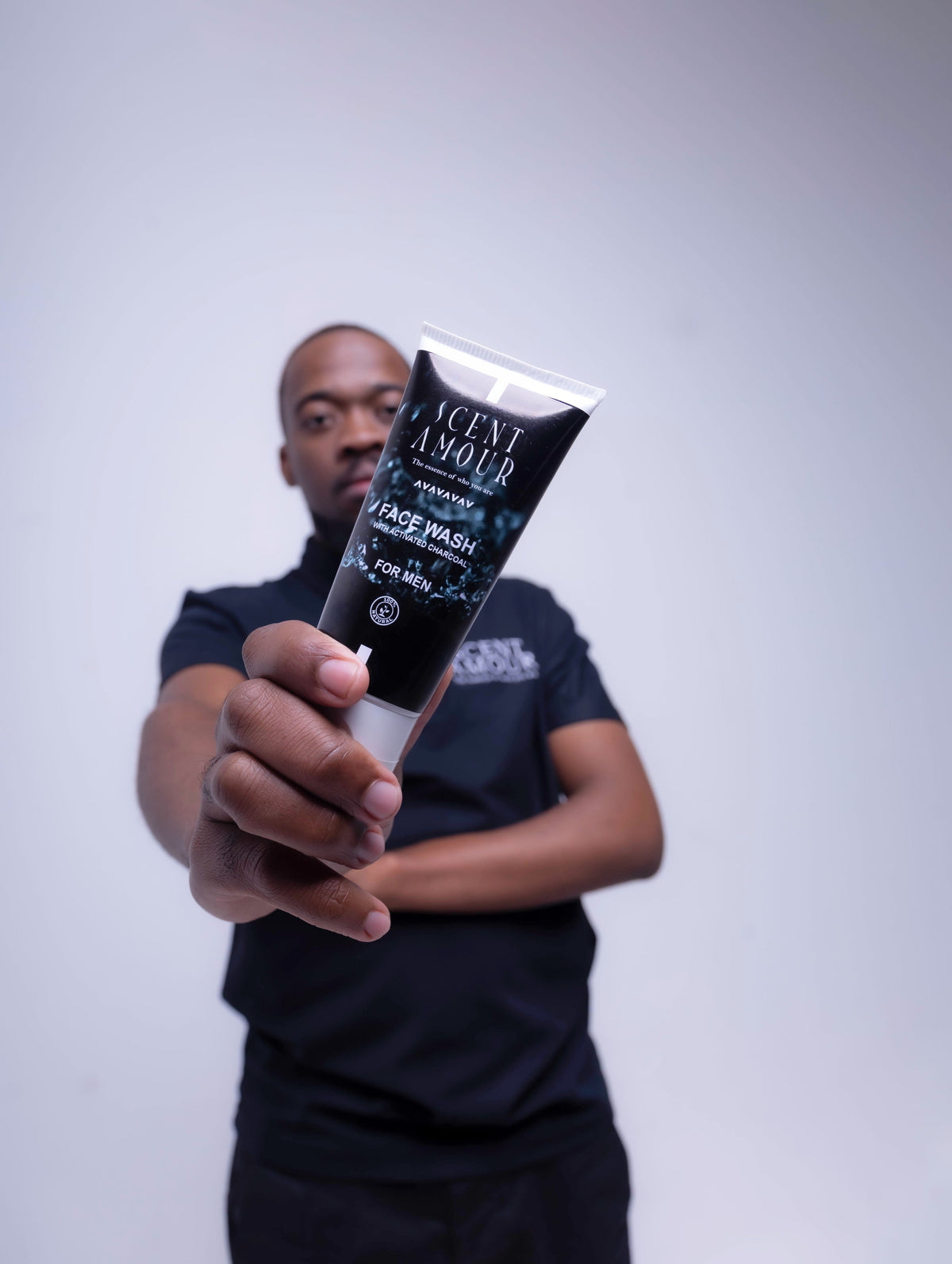 Person holding a tube of 'Scent Amour' face wash against a plain background